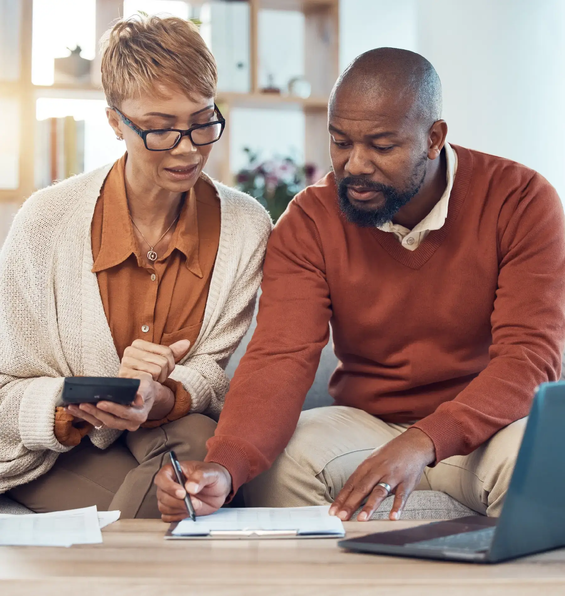 Middle-aged couple sitting together on a couch in a well-lit living room, reviewing financial documents.